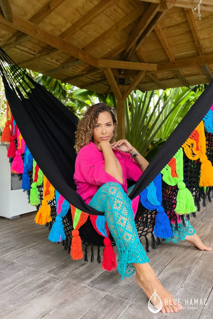 hamac noir avec des franges et pompons multicolores large elegant et confortable mathilda crampon dans le hamac sous une terrasse couverte en guadeloupe